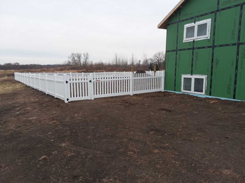White vinyl picket fence surrounding a newly constructed home without siding