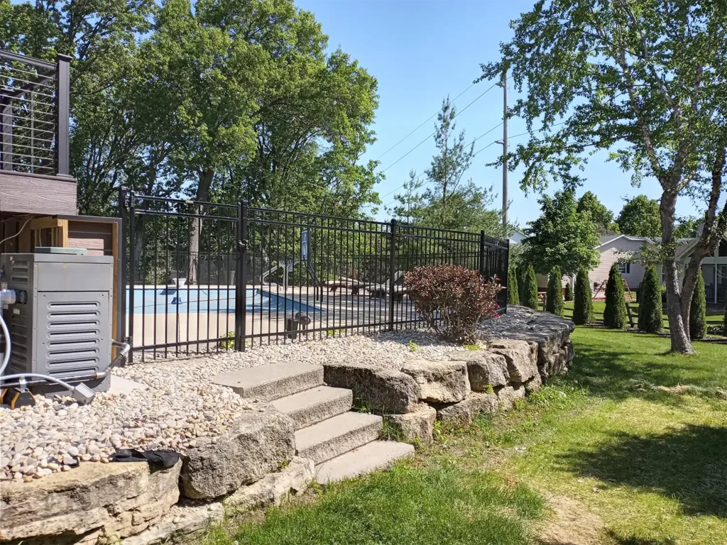 Black ornamental steel fence along a pool side with a set of stairs and large landscaping rocks